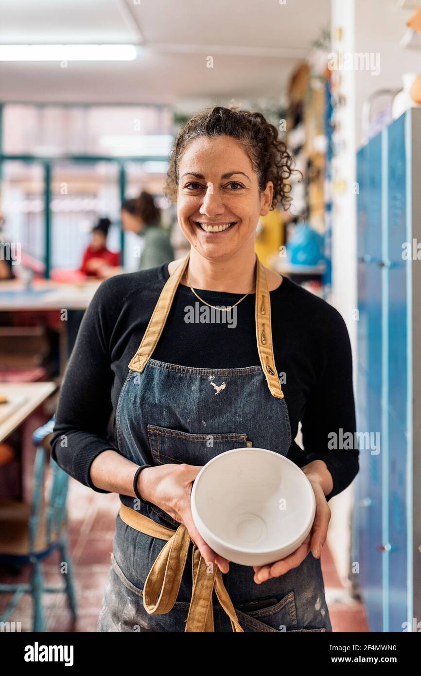 Stock photo of smiley woman wearing apron holding ceramic piece ...