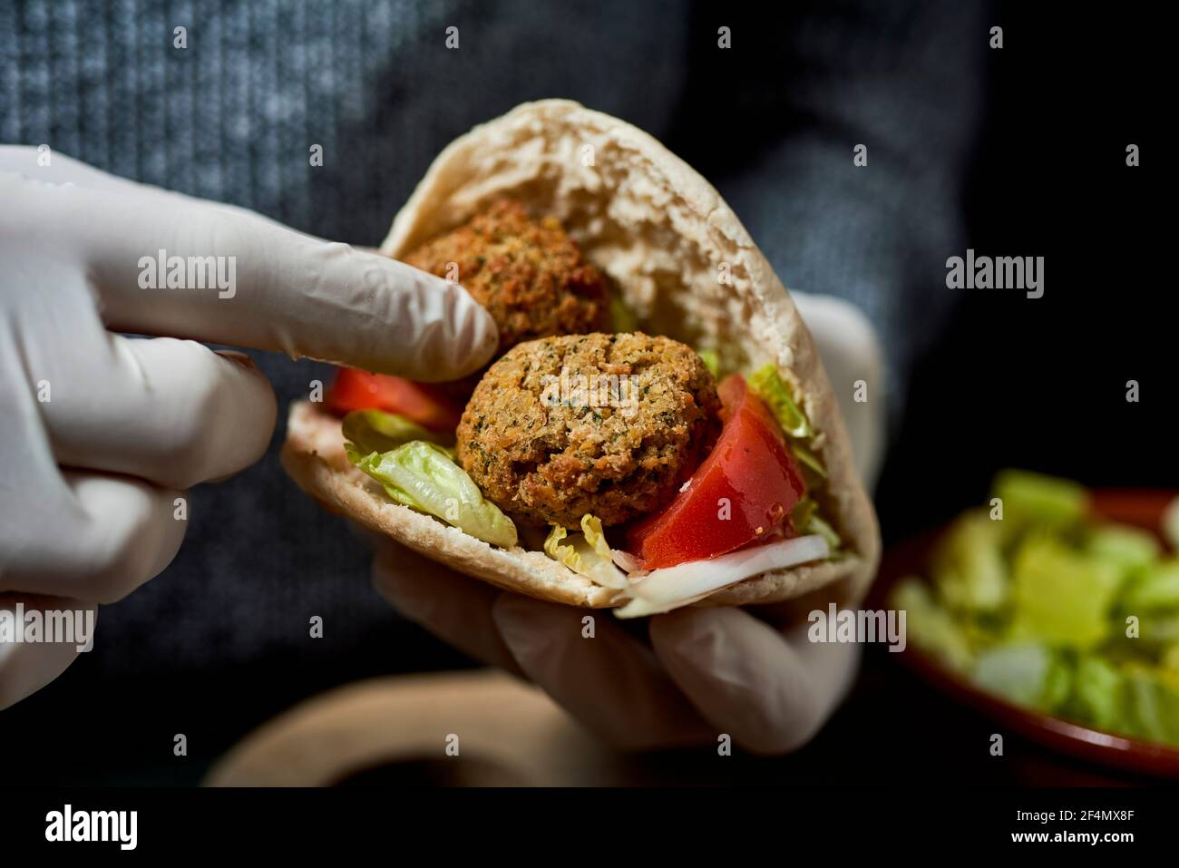 young man, wearing latex gloves, fills a pita bread with some falafel Stock Photo