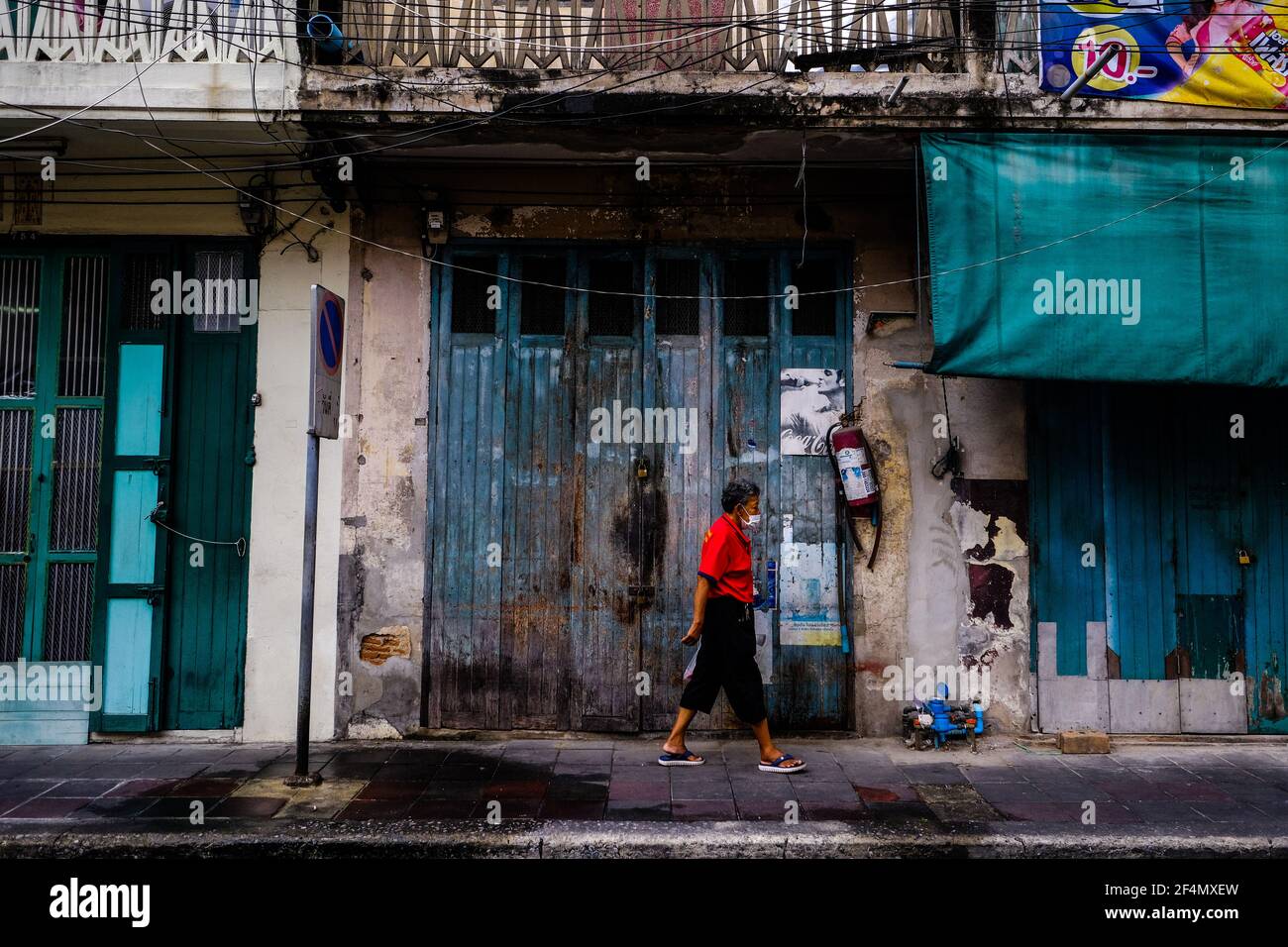 A woman in a bright red shirt walks past some old buildings in the Chinatown area of Bangkok, Thailand Stock Photo
