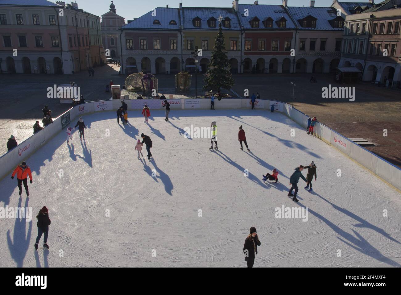 Zamosc, Poland, December 27, 2020. Townspeople skate on an ice skating rink on a sunny winter morning. Skating rink in the central square of the city. Stock Photo