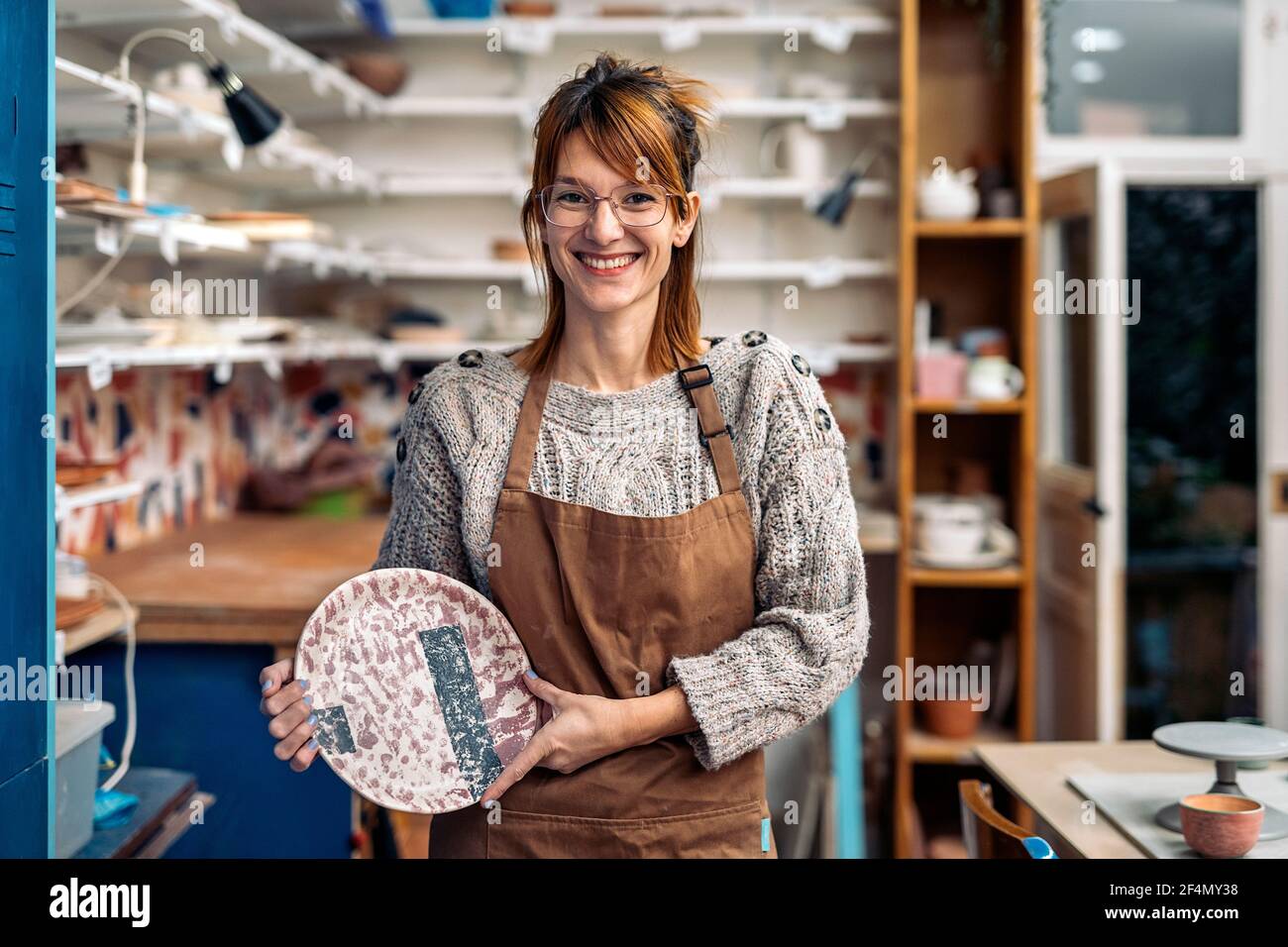 Stock photo of smiley woman wearing apron holding ceramic piece ...