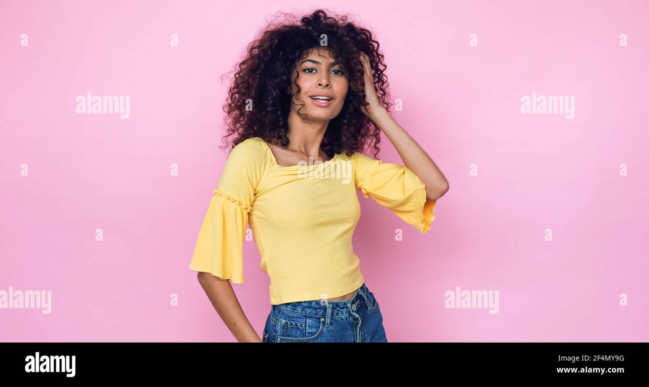 young model posing and adjusting curly hair isolated on pink Stock Photo