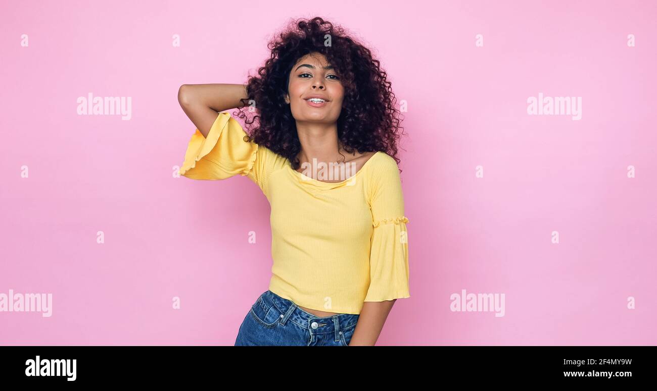 cheerful young model posing and adjusting curly hair on pink Stock Photo