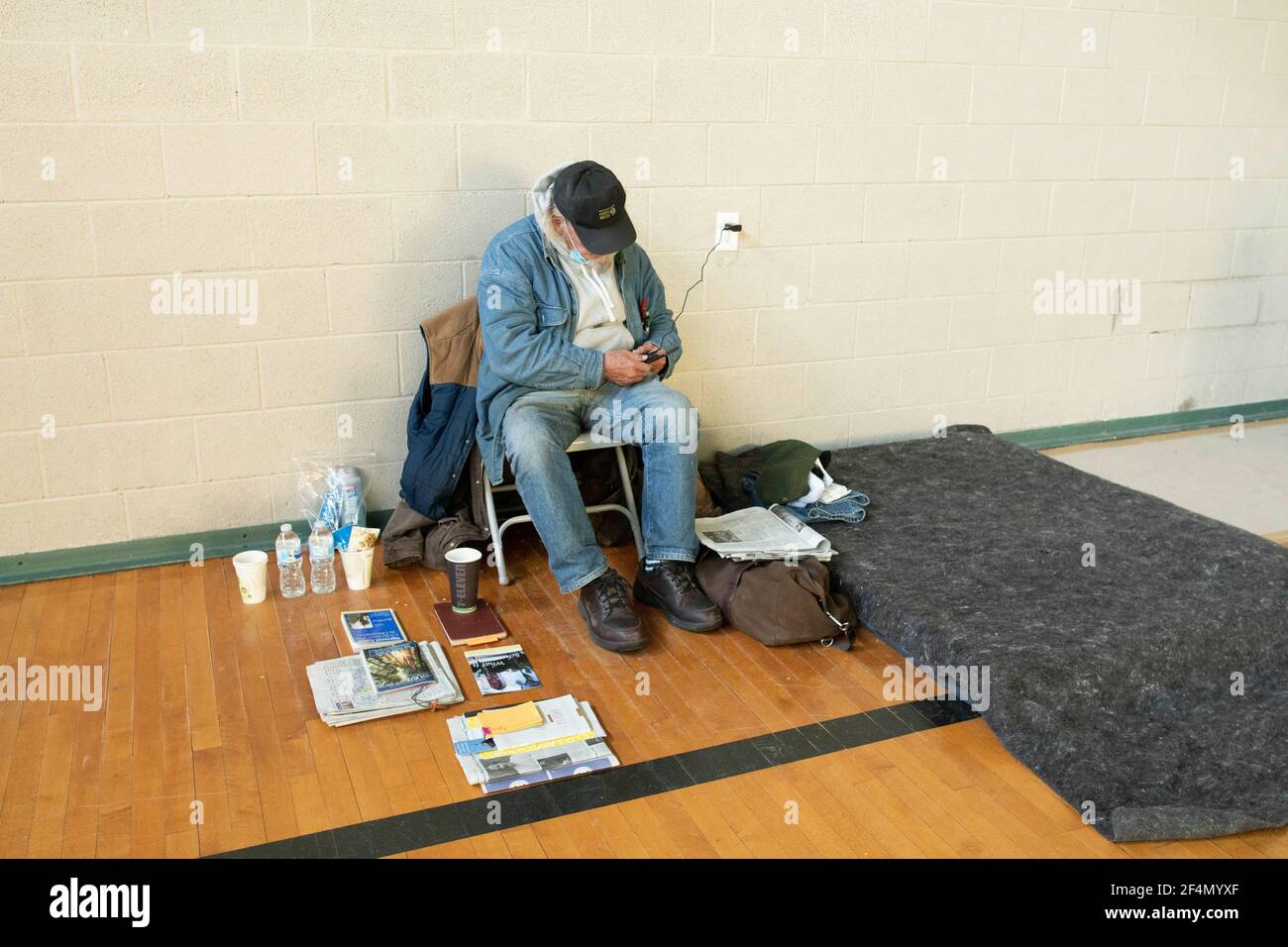 Austin, TX USA  Feb 20, 2021: A homeless guest man who stayed all week in a church shelter during the epic Texas snowstorm of 2021 charges his cell phone by his sleeping mat. Texas reported 57 deaths statewide due to the heavy snow and days of below-freezing temperatures, both unusual in this part of the country. ©Bob Daemmrich Stock Photo