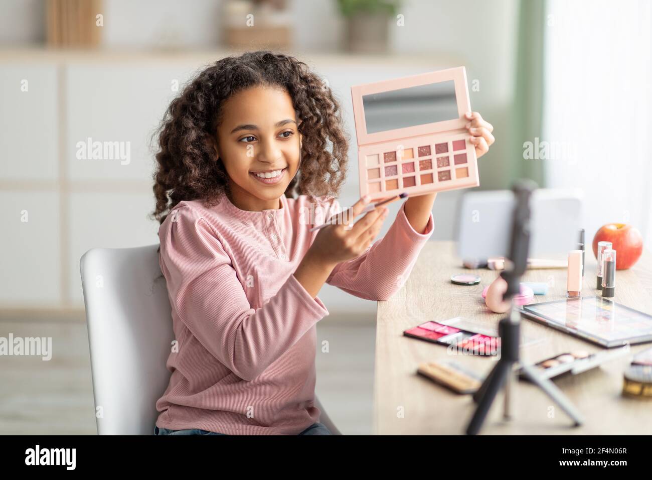 Beauty blog. Black teenage girl doing makeup and recording vlog on phone Stock Photo