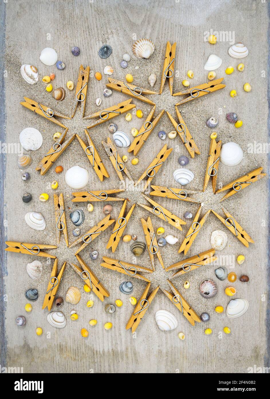 Starfish shapes made with clothes pegs, with sea shells and sand over weathered white board. Stock Photo