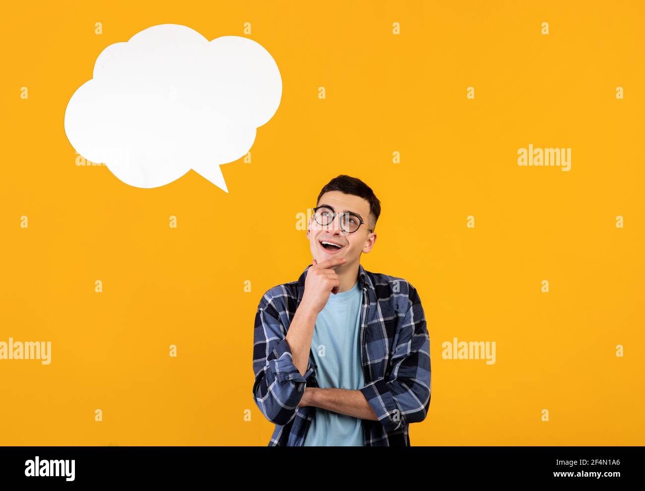 Thoughtful young guy looking at empty speech bubble over orange studio background, mockup for design Stock Photo