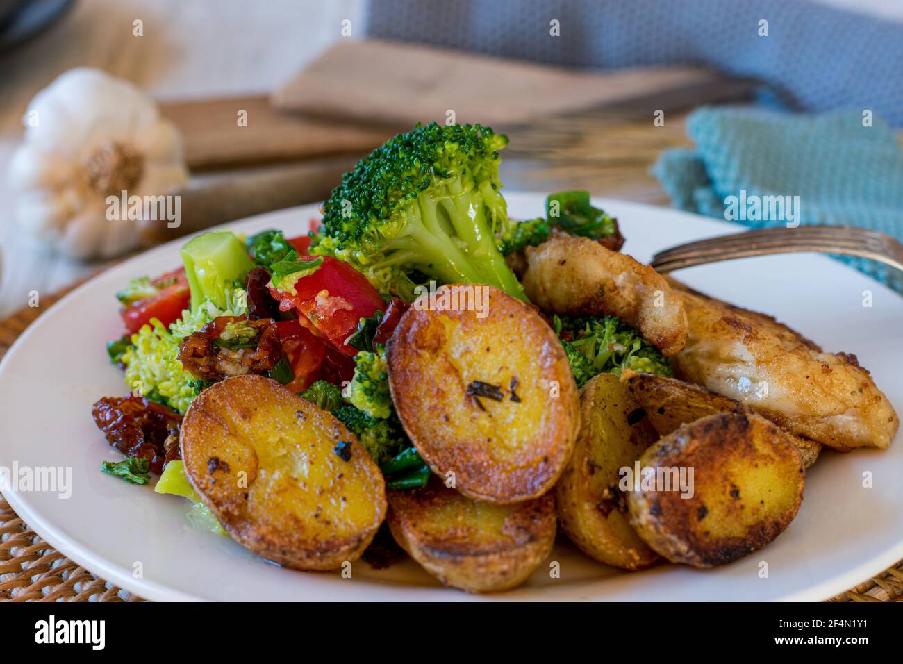 mediterranean broccoli salad and roasted rosemary potatoes served as a side dish on a plate with fried fish Stock Photo