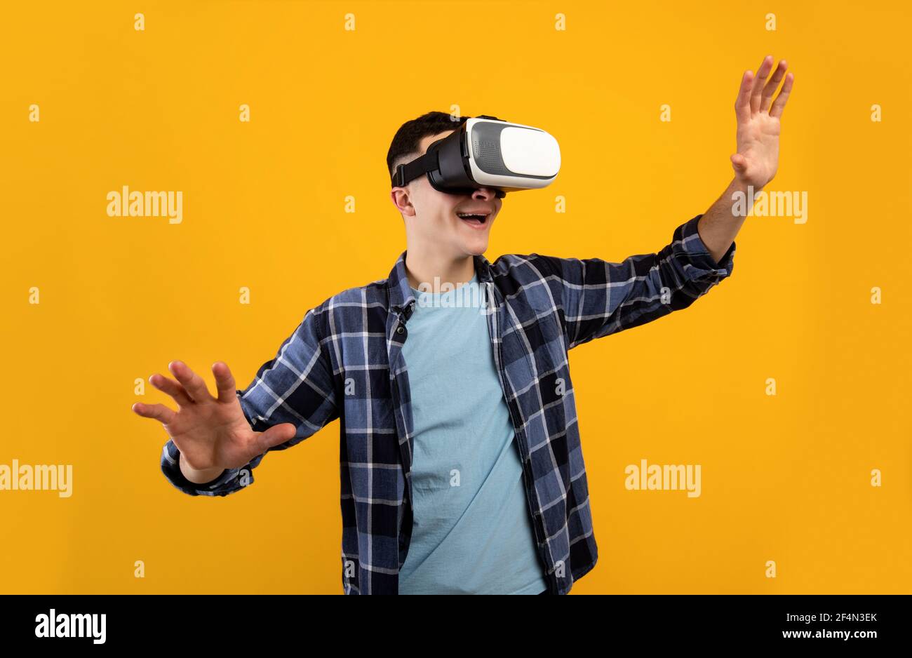 Joyful young guy using virtual reality headset, controlling cyber environment with moving gestures on orange background Stock Photo