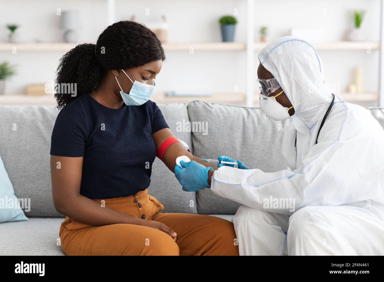 Doctor in protective suit taking blood sample for female patient Stock Photo