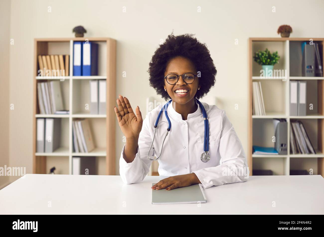Friendly smiling african american woman doctor welcoming sit at desk in office Stock Photo