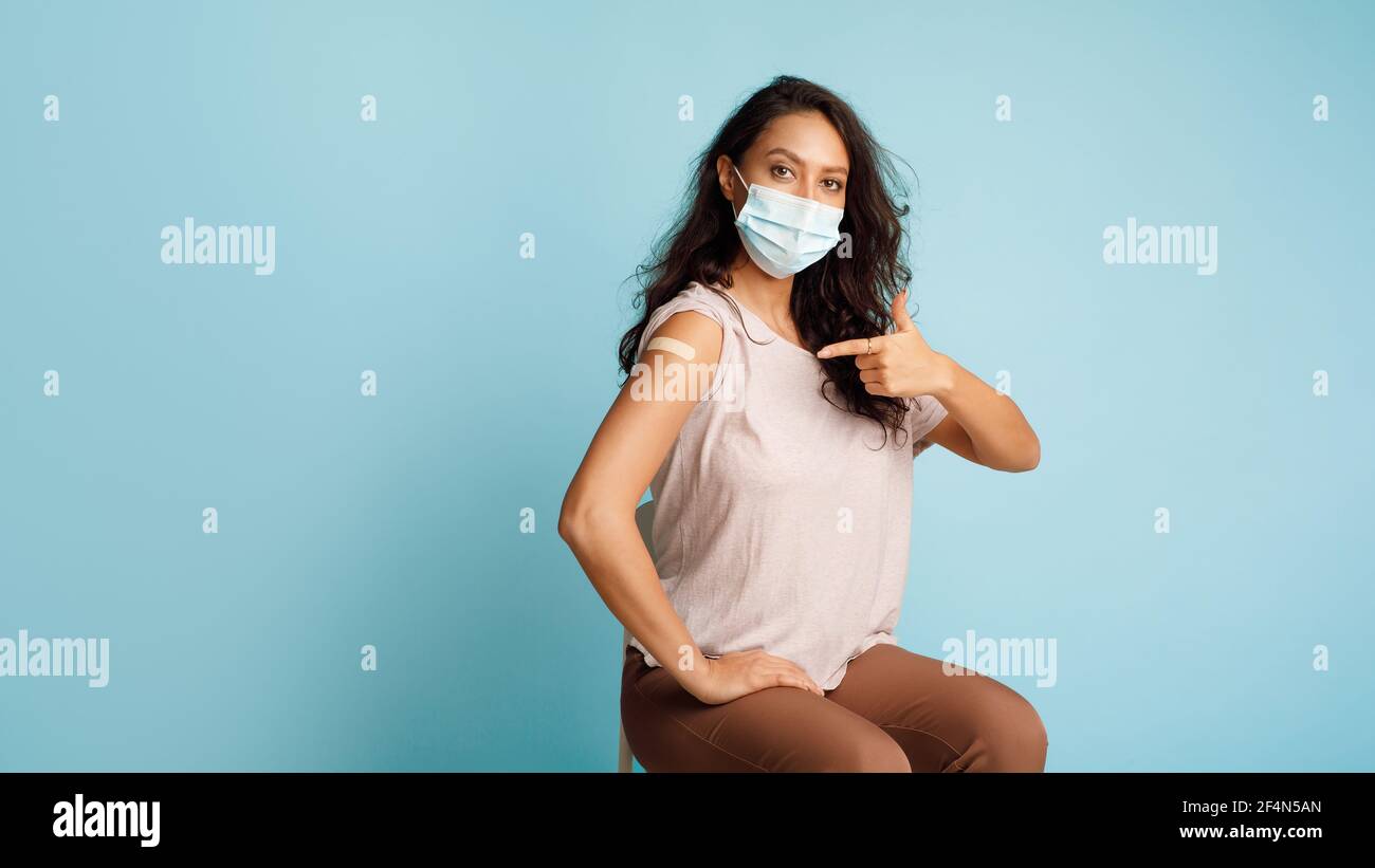 Vaccinated Woman Pointing At Arm After Vaccine Injection, Blue Background Stock Photo