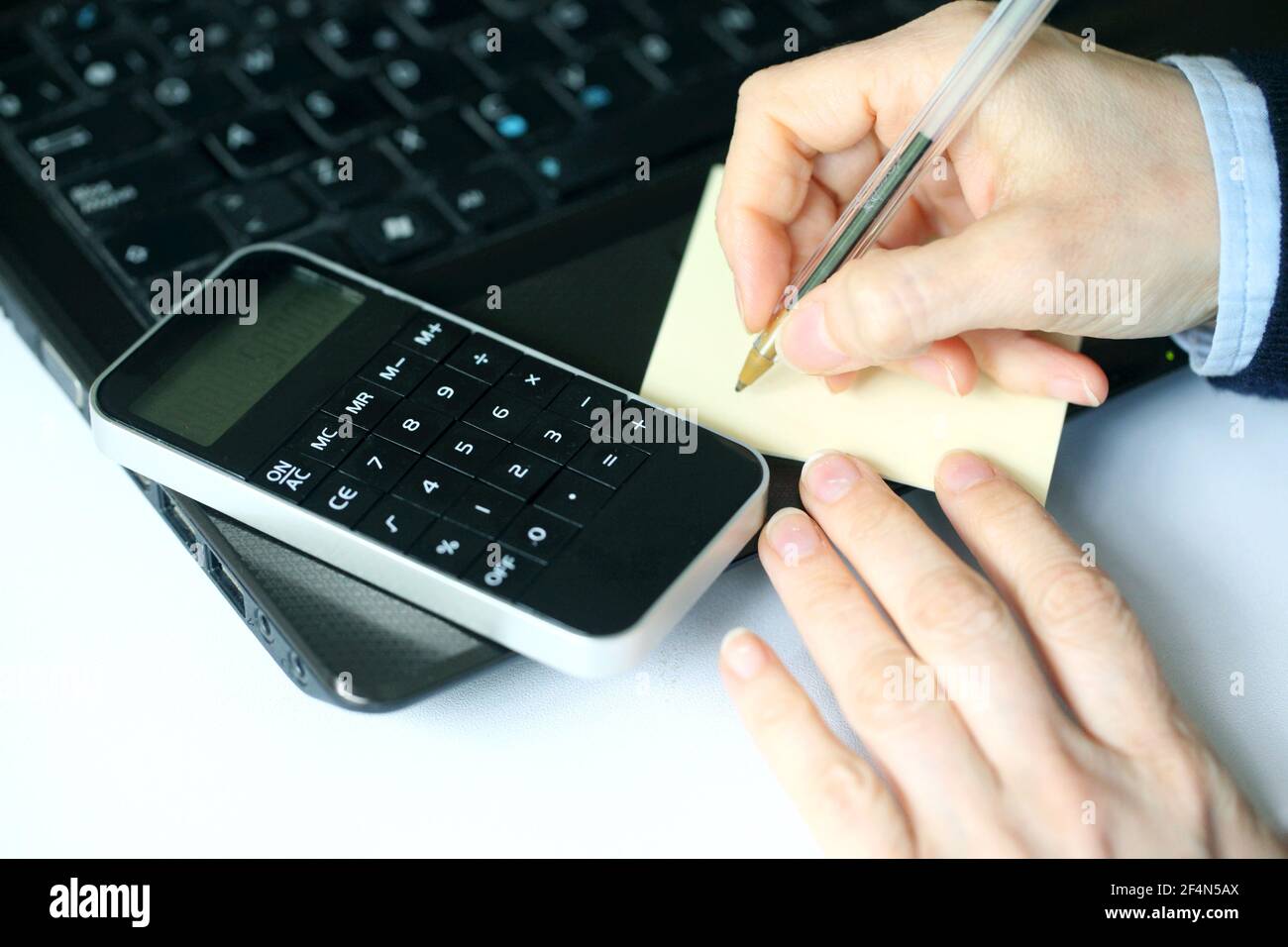Closeup of a hand holding a pen over blank paper with calculator and laptop Stock Photo