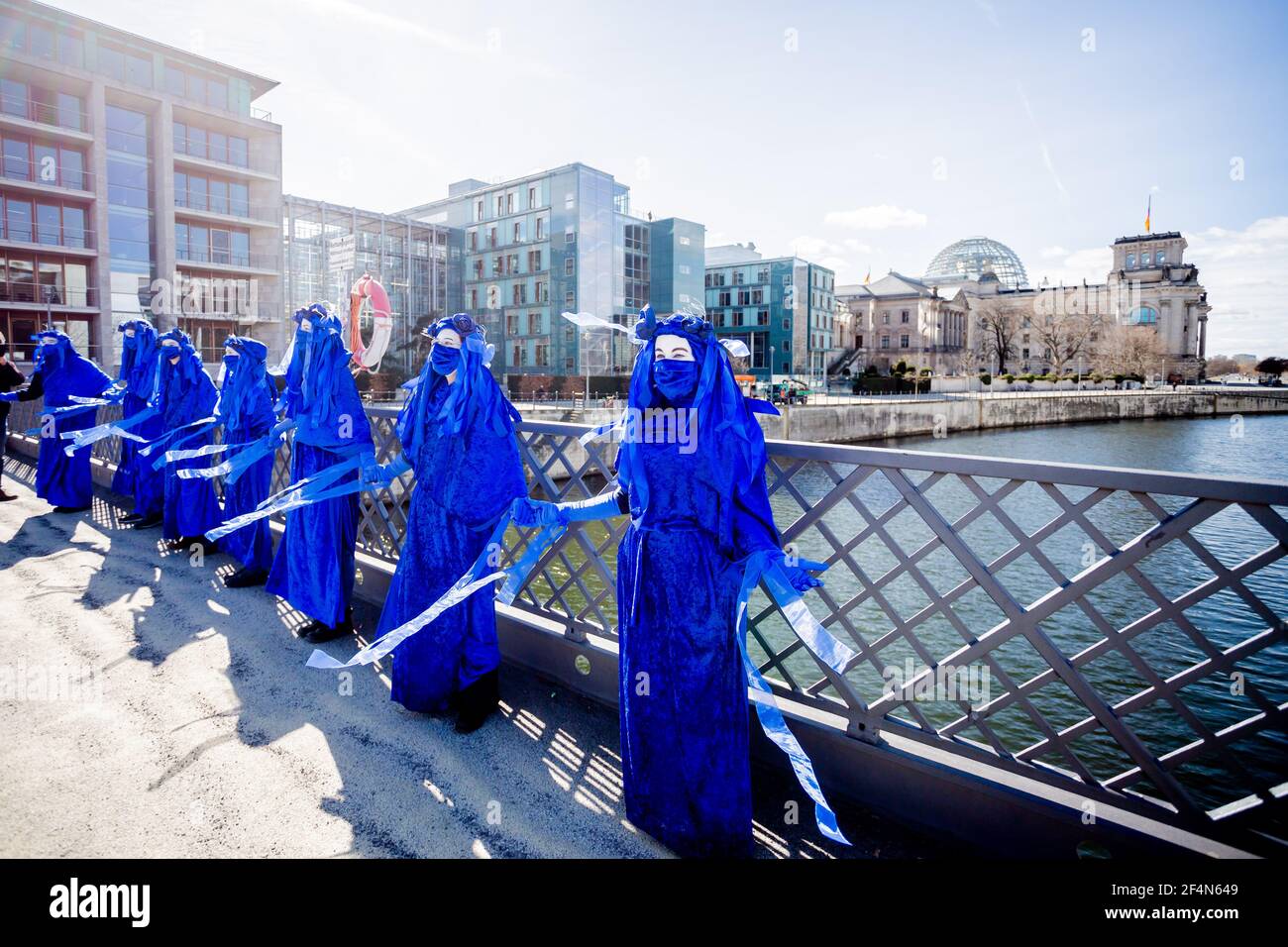 Berlin, Germany. 22nd Mar, 2021. People dressed as 'Blue Rebels' stand on the Marschall Bridge during a performance of the environmental protection movement 'Extinction Rebellion' on the occasion of World Water Day under the motto 'Protect water - stop fracking worldwide'; the Reichstag building can be seen in the background. Credit: Christoph Soeder/dpa/Alamy Live News Stock Photo