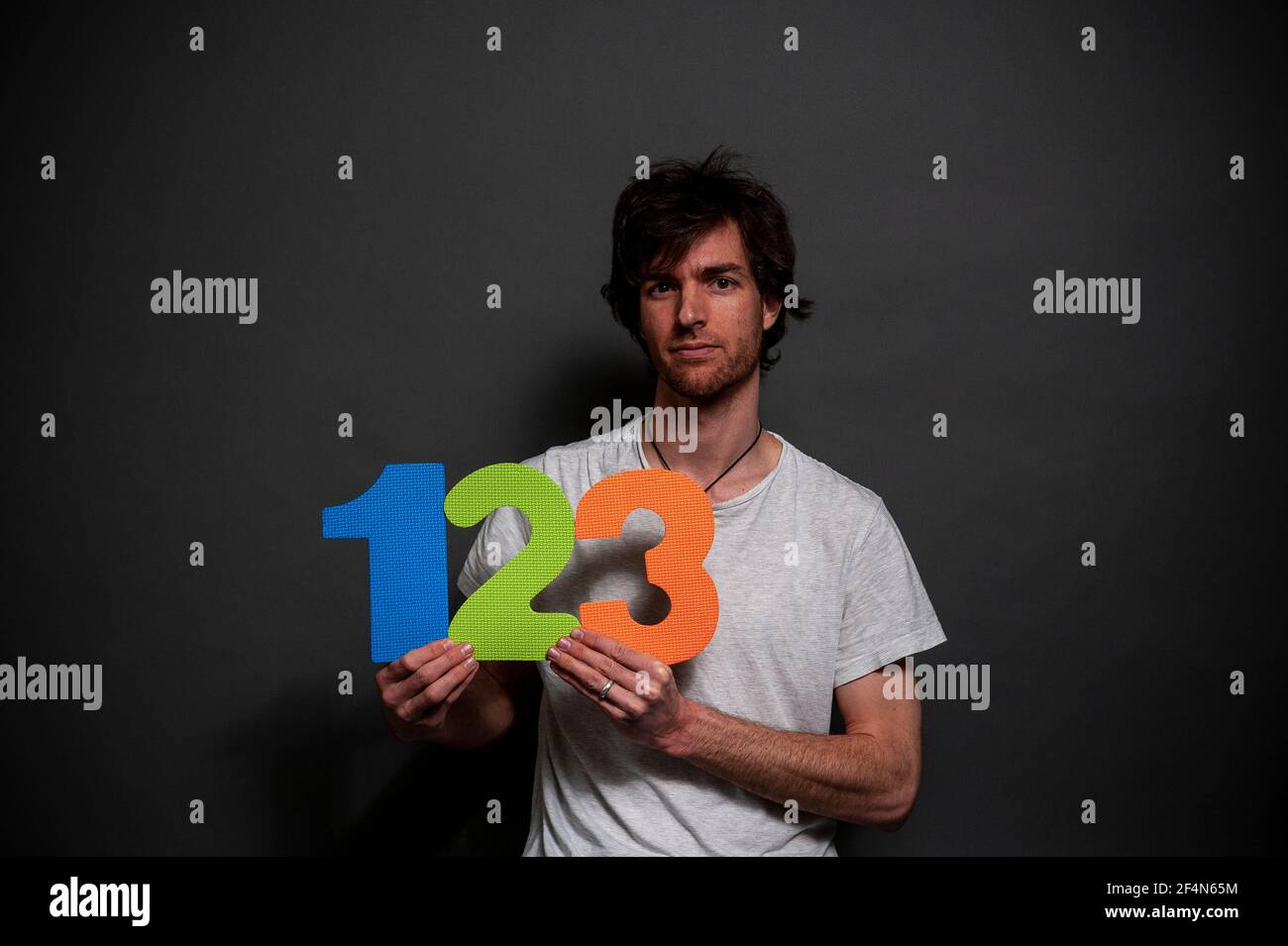 A young man wearing a white t-shirt holding up colourful foam numbers 1, 2 and 3. Stock Photo