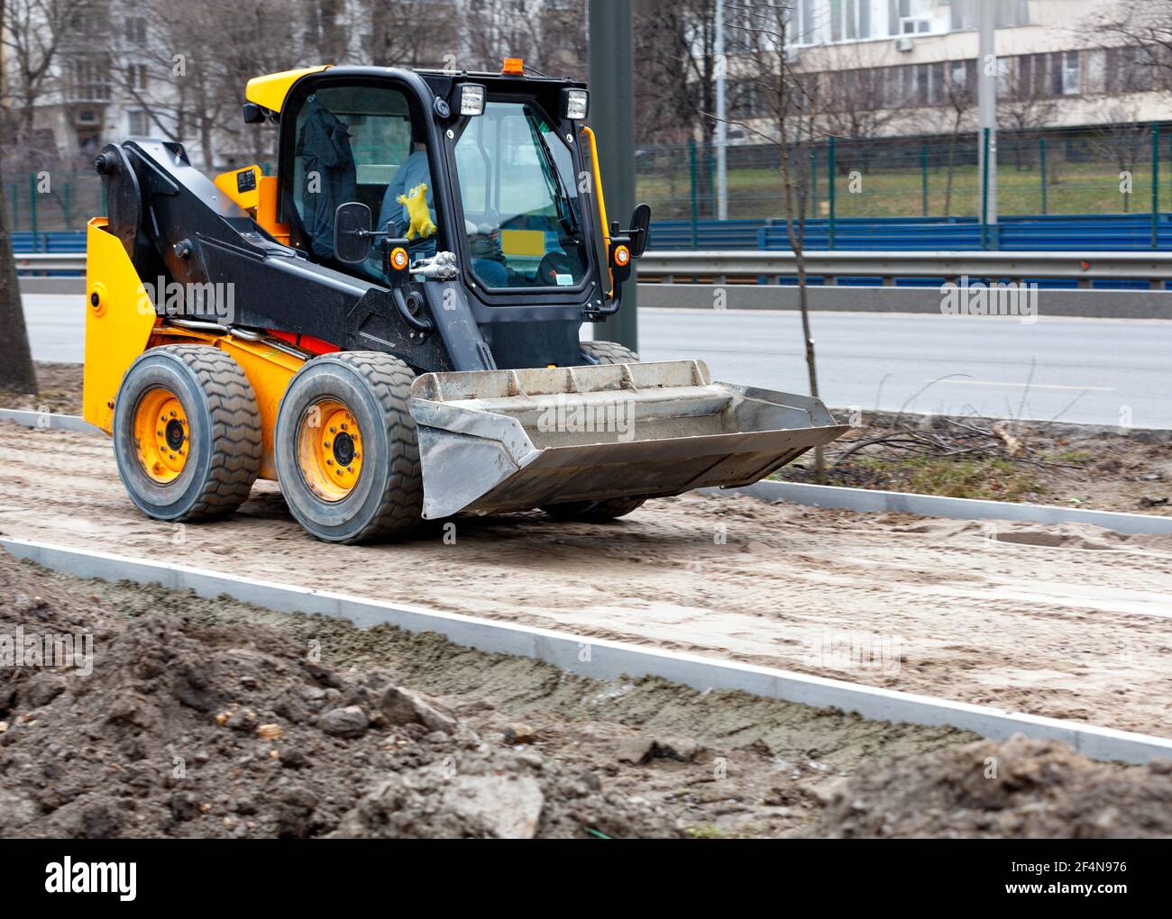 Compact road grader on a construction site is leveling a sandy base on