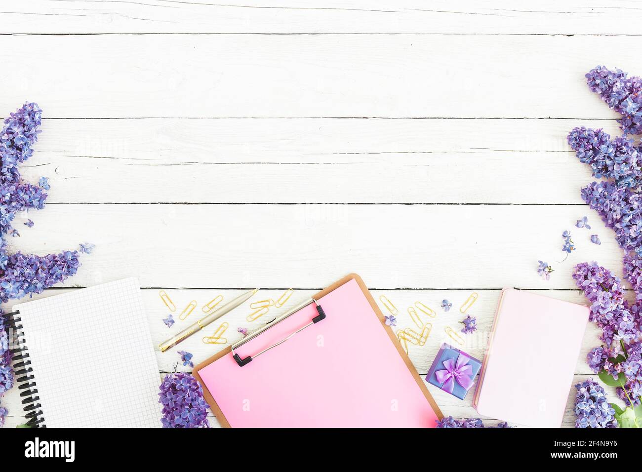 Clipboard, diary, lilac flowers and accessories on white wooden