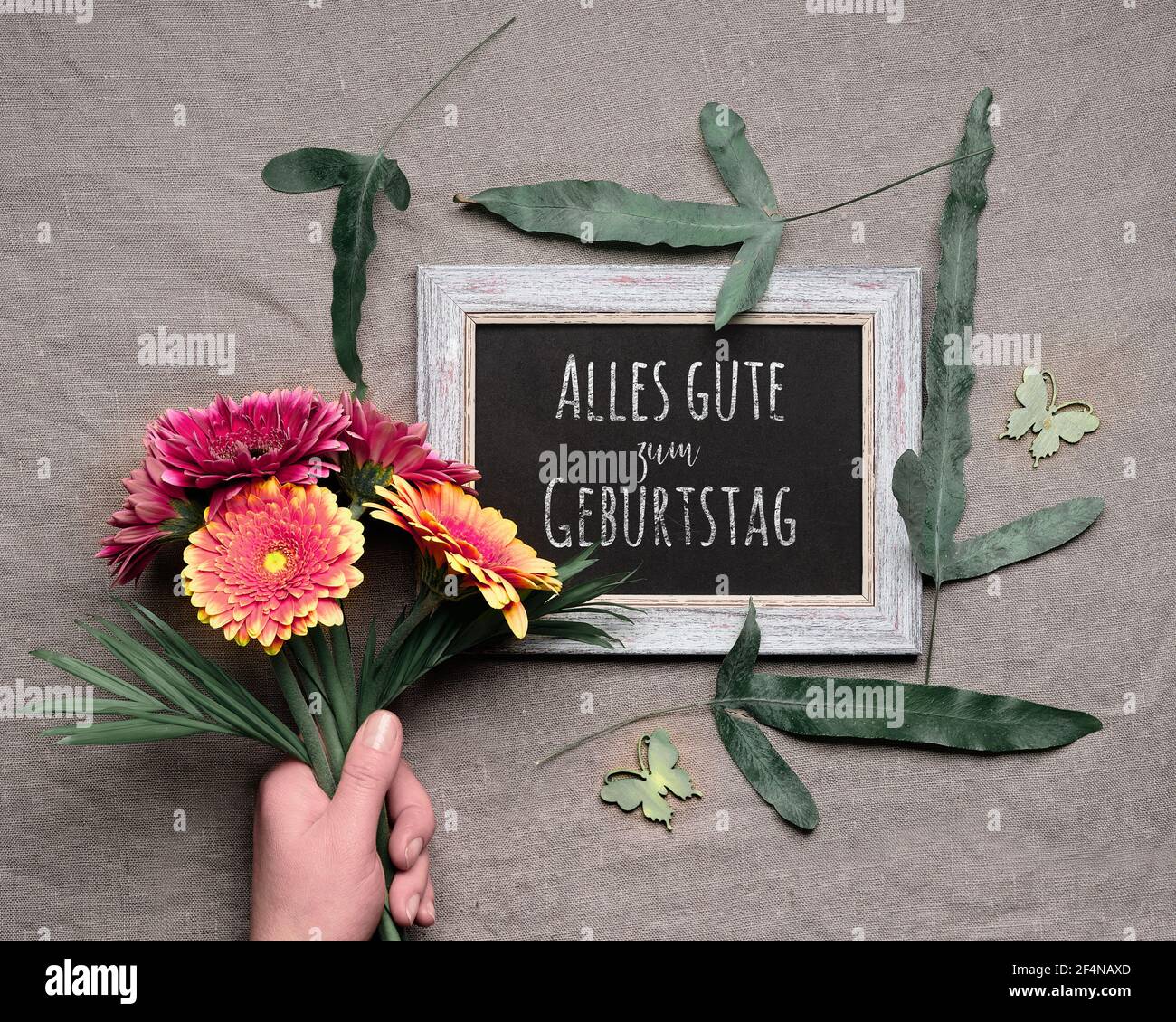 German text Alles gute zum Geburtstag on blackboard means Happy Birthday. Springtime background. Hand hold bunch of vibrant gerbera flowers, exotic Stock Photo