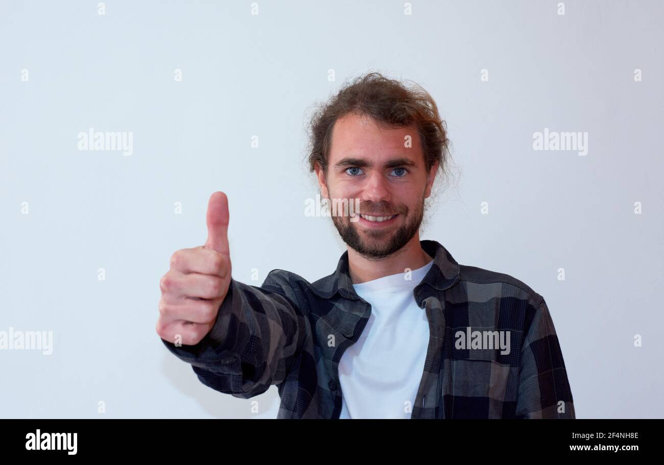 Closeup of a Spanish young bearded cheerful male giving thumbs up on the white background Stock Photo