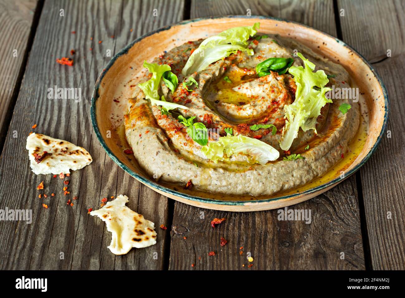 An oriental dish of baked eggplant babaganush (eggplant puree) with spices, herbs, lettuce and oriental flatbreads on wooden background. Stock Photo