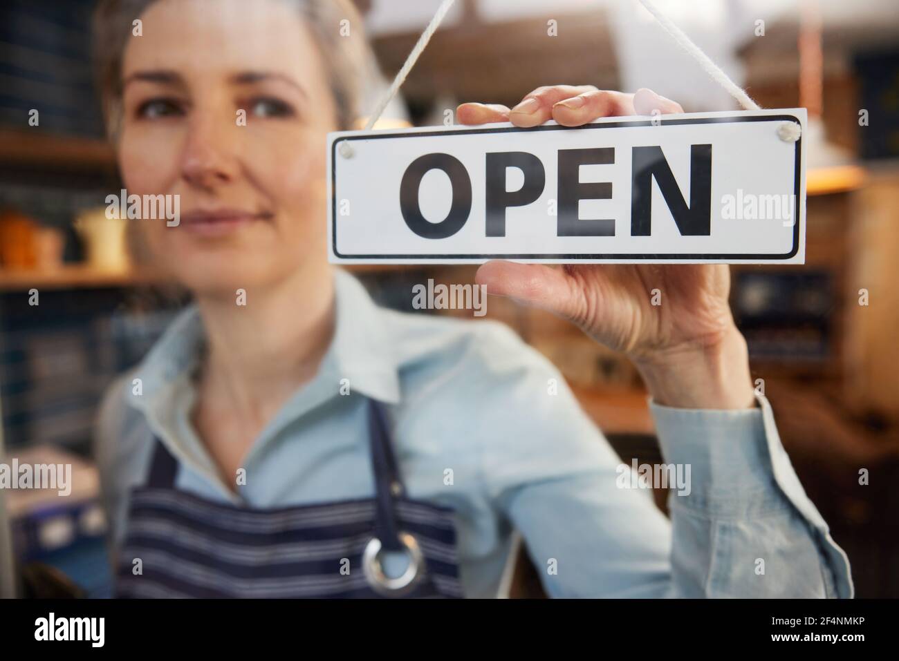Female Small Business Owner Turning Around Open Sign On Shop Or Cafe Window Or Door Stock Photo