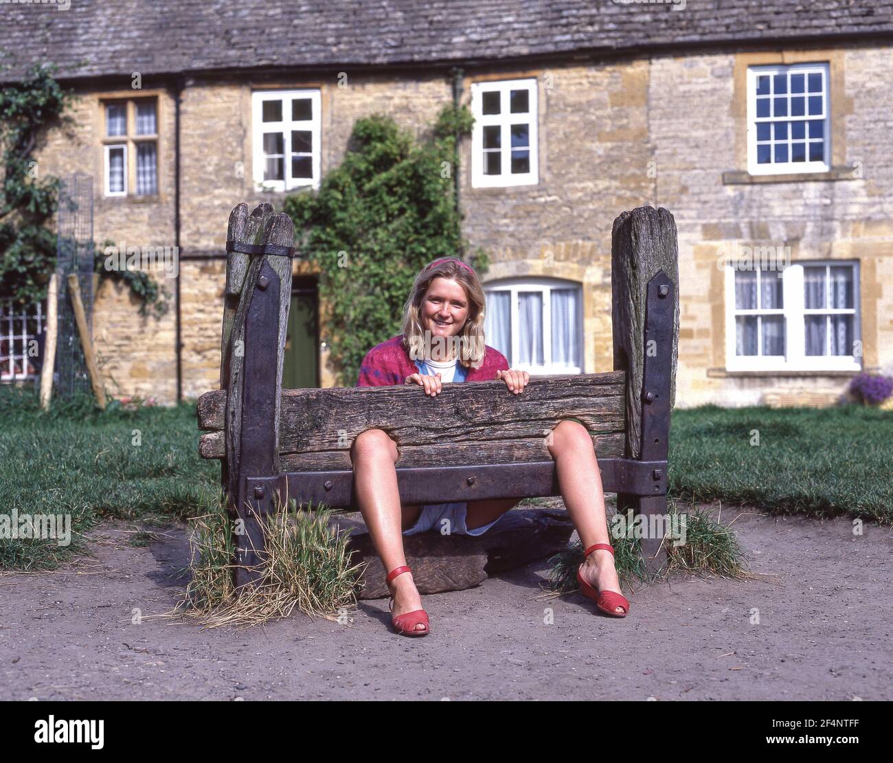 Young woman posing in village stocks, Market Square, Stow-on-the-Wold, Gloucestershire, England, United Kingdom Stock Photo
