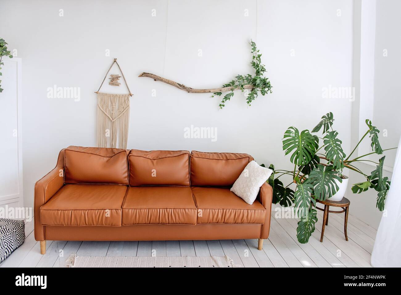 Stylish, trendy interior in Scandinavian style. In the white loft room  there is brown leather sofa, green monster, driftwood with ivy hangs on the  wal Stock Photo - Alamy