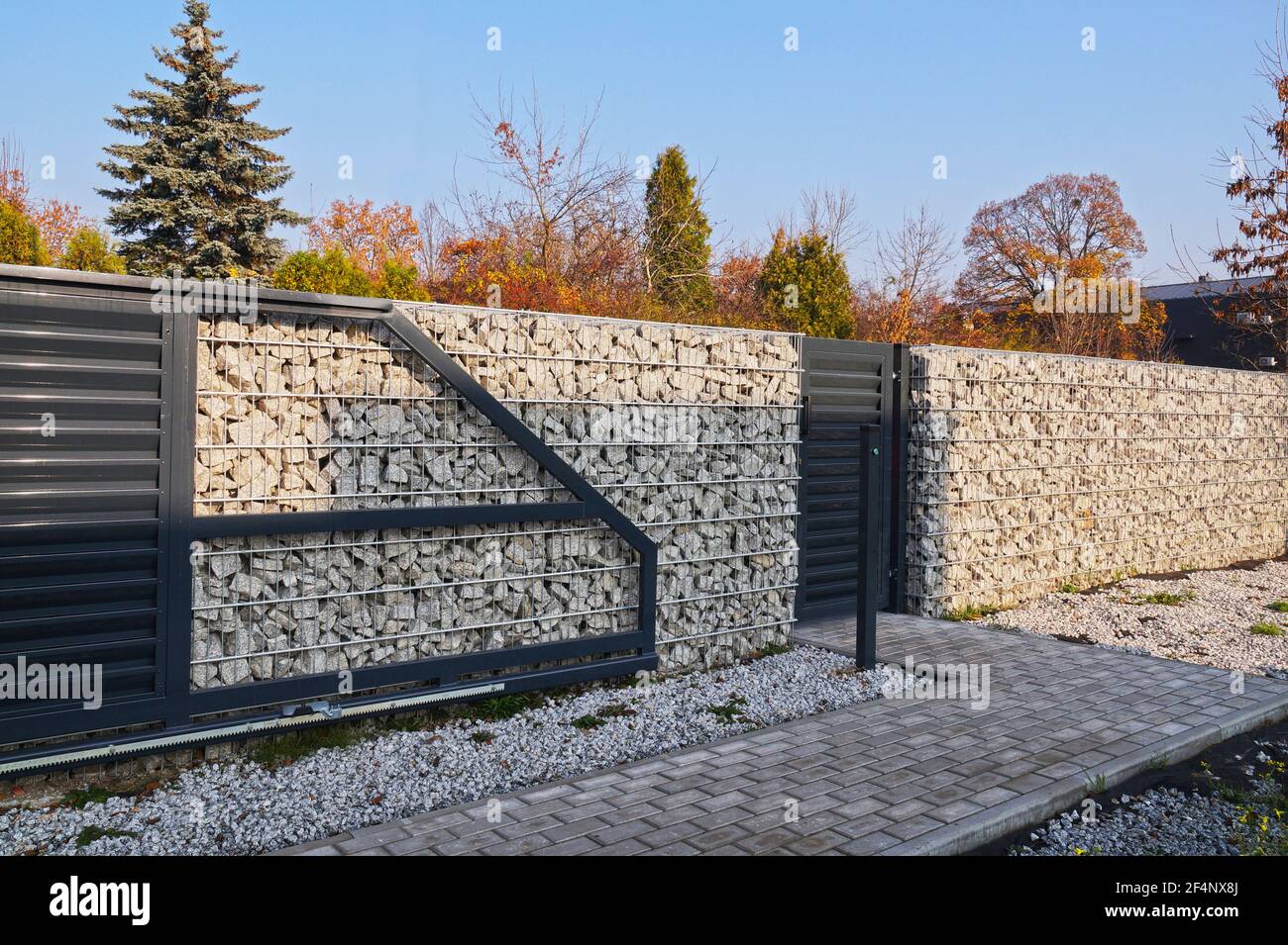 Automatic entrance gate and wicket integrated into the wall made of a gabion. A fence made of gabions. Stock Photo