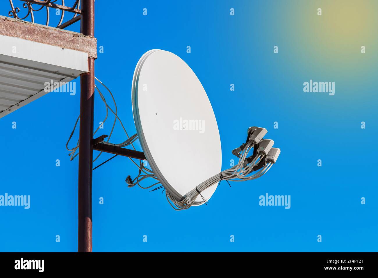 Satellite dish on a part of a building against a blue sky with sunlight and glare. Stock Photo