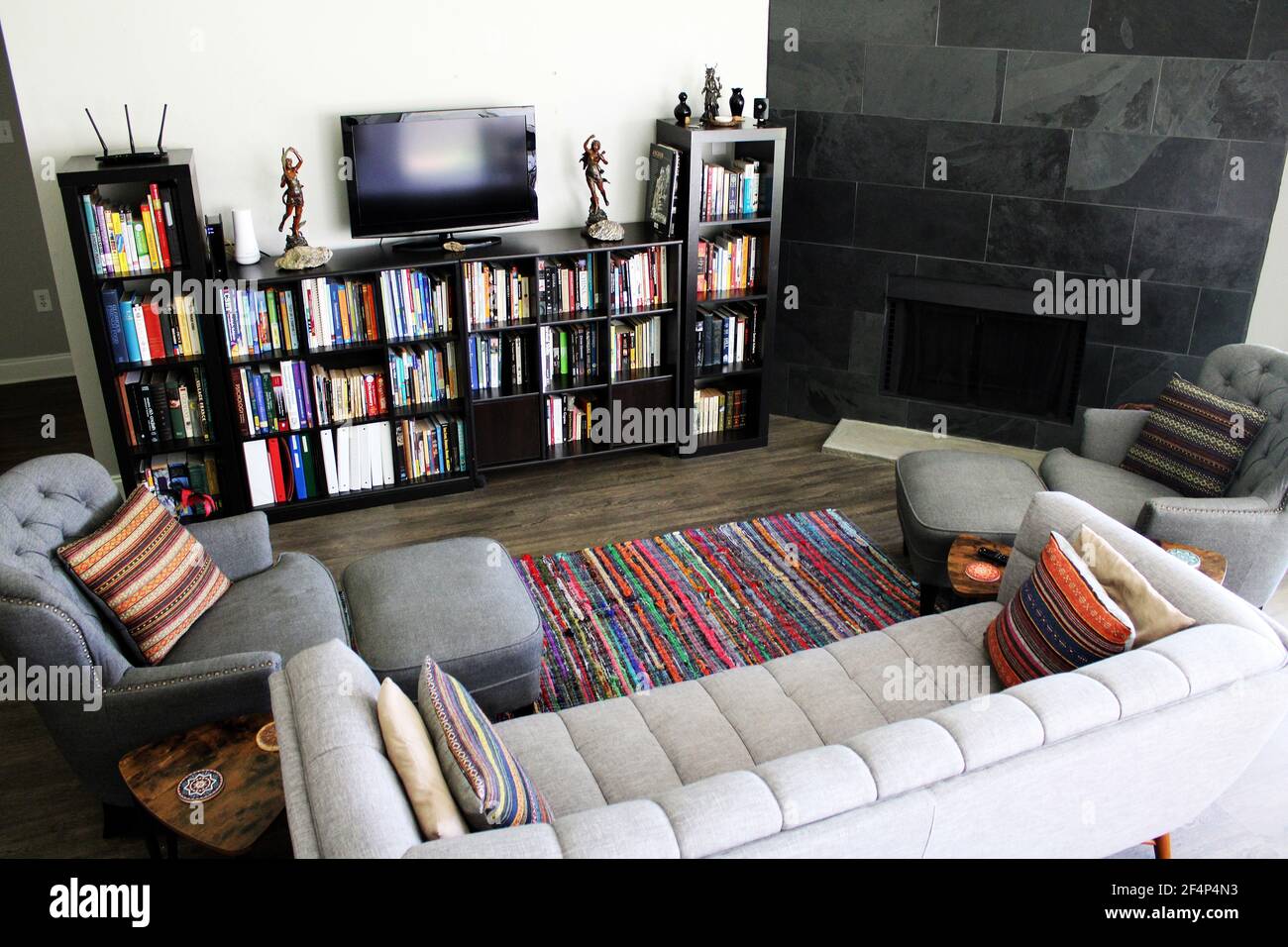 my grey living room features a large fireplace, small library, and pops of color throughout Stock Photo