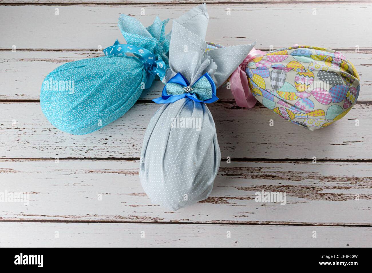 Chocolate Easter eggs packed with colorful fabrics and bows on a white wooden table. Stock Photo
