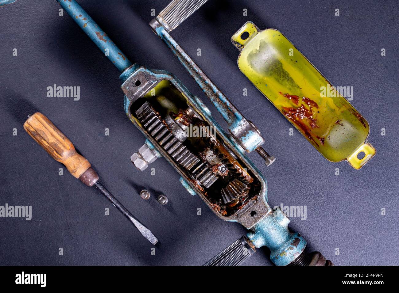 The cover was removed from the gearbox in an old hand drill. Servicing of tools for work in a carpentry workshop. Dark background. Stock Photo