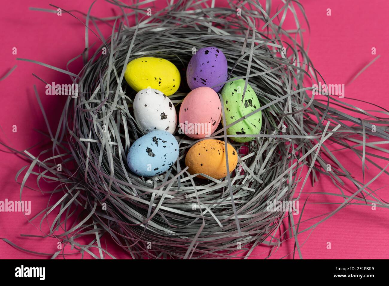 Colorful eggs in a handmade basket on pink background. Creative eastern background Stock Photo