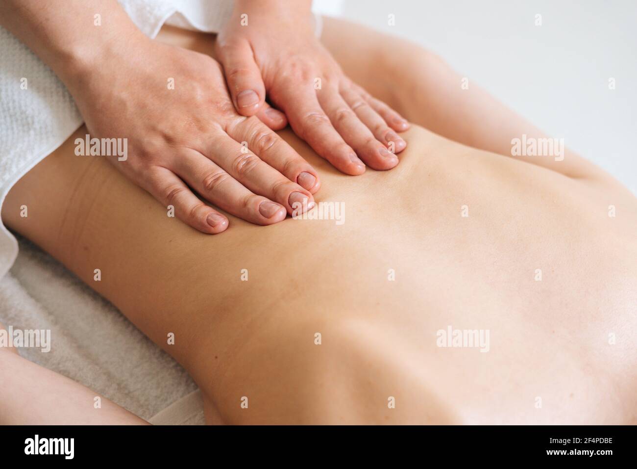 Top view of male masseur massaging back of young unrecognizable woman lying on massage table. Stock Photo
