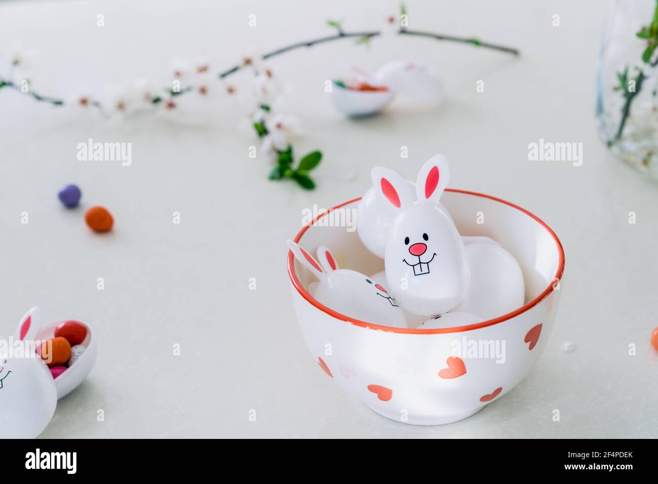 Funny Easter eggs containers filled with candy and chocolate eggs with bunny ears in a bowl on the white kitchen table. Festive spring Easter Stock Photo