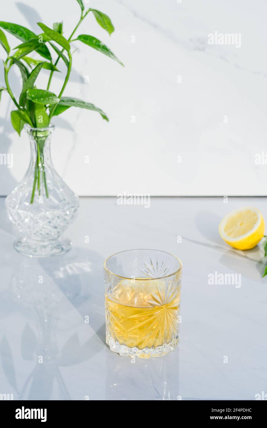 Crystal glass with yellow cocktail, vase with fresh greenery and half