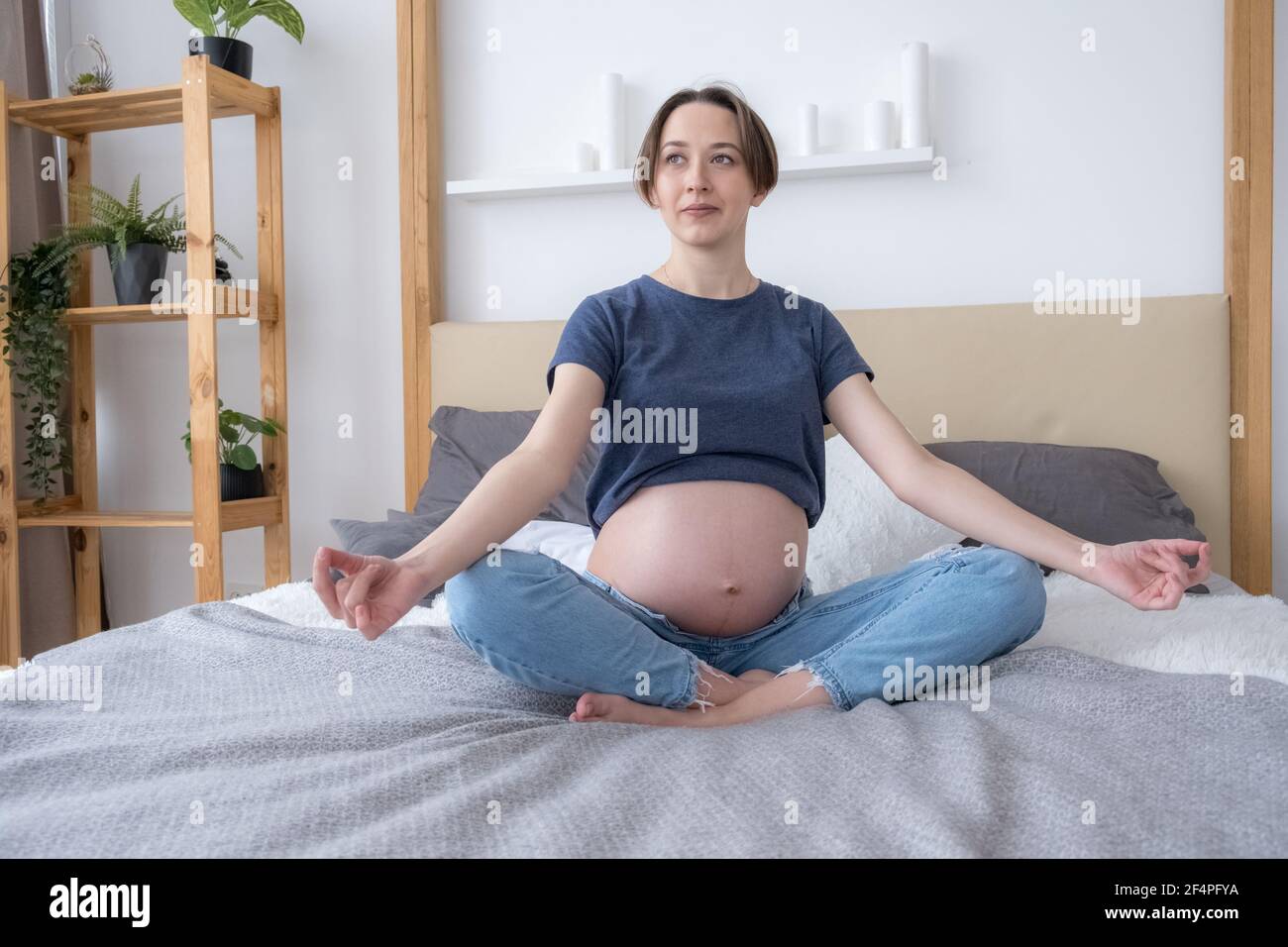 Front view of pregnant woman sitting in bed in Lotus position practicing meditation, concept HLS, yoga Stock Photo