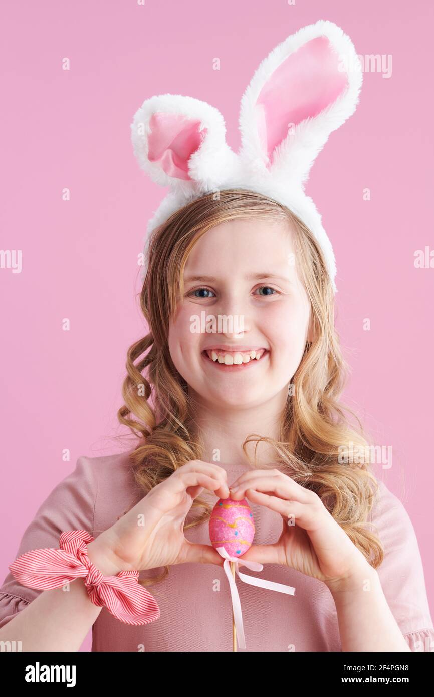 Portrait of happy modern child with long wavy blond hair with bunny ears and easter egg isolated on pink. Stock Photo