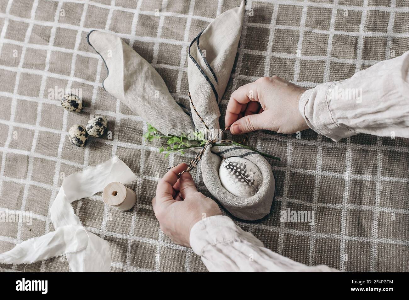Closeup of womans hands folding napkins. Easter decorative table setting. Spring still life with quail and hen eggs. Beige linen table cloth Stock Photo