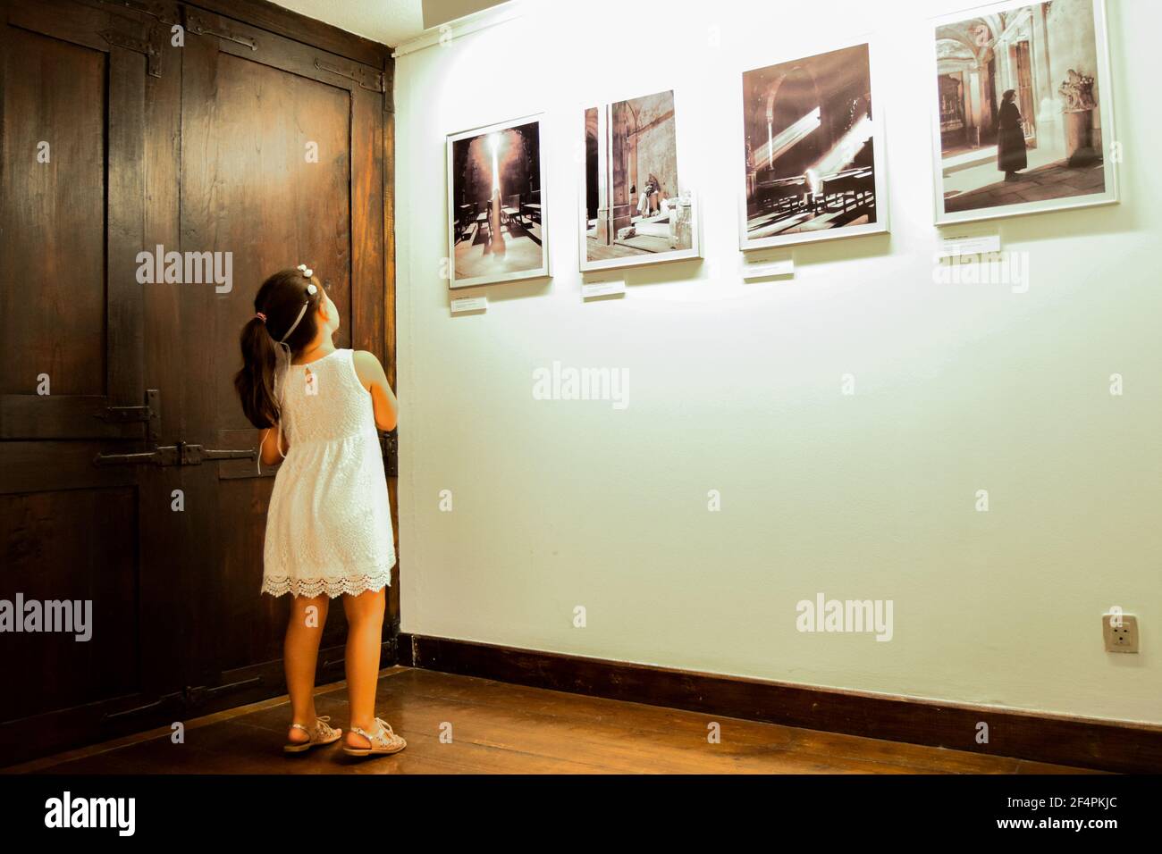 Little girl in white dress looking at historical photographs in museu exposition. Cultural learning, old and new interactions. History education. Stock Photo