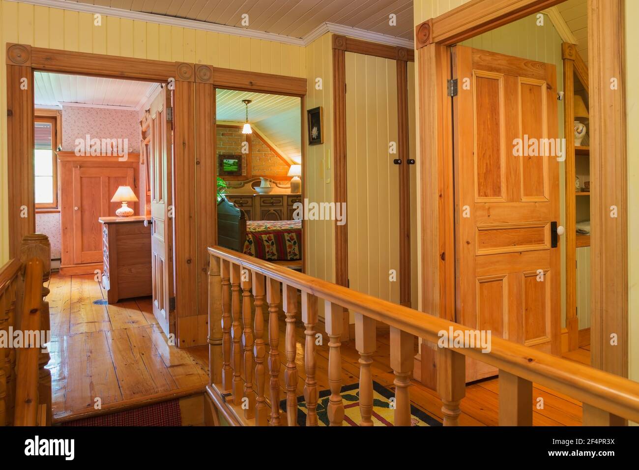 Hallway and opened doors of guest bedrooms and bathroom, maple wood staircase railing on upstairs floor with Eastern Hemlock floorboards in old home Stock Photo
