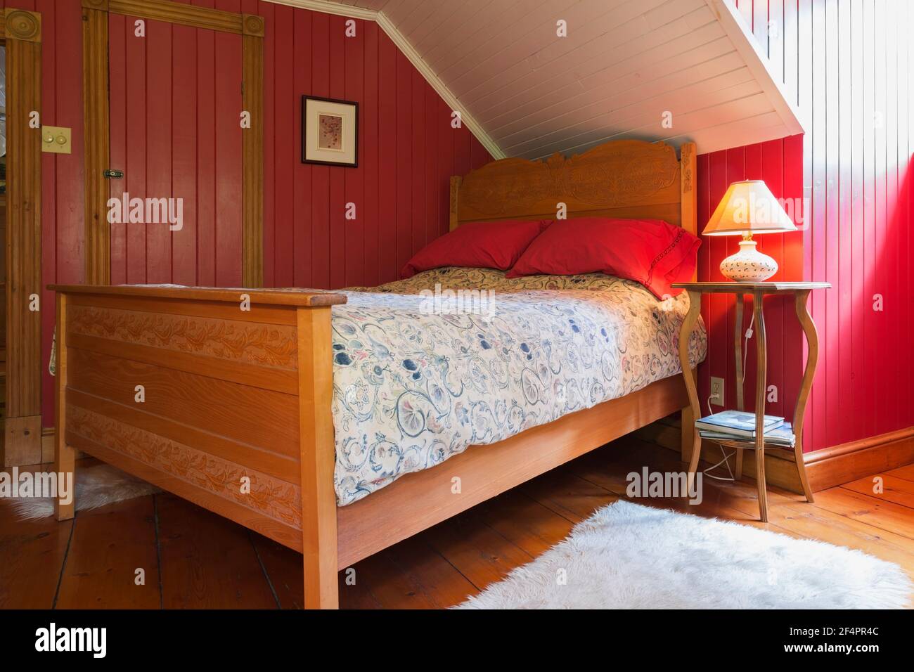 Double bed on elm wood frame with pressed design elements on headboard and footboard, maple wood nightstand and red and white painted guest bedroom Stock Photo