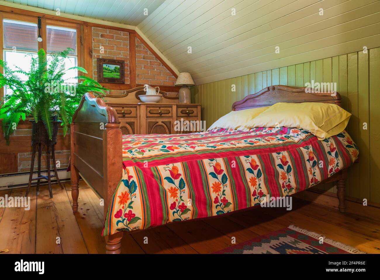 Double bed with stained maple wood headboard and footboard and red flowery bedspread, antique