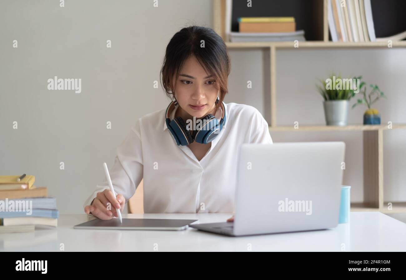 Portrait of female worker working from home with digital tablet, laptop and headphone in home office room. Stock Photo