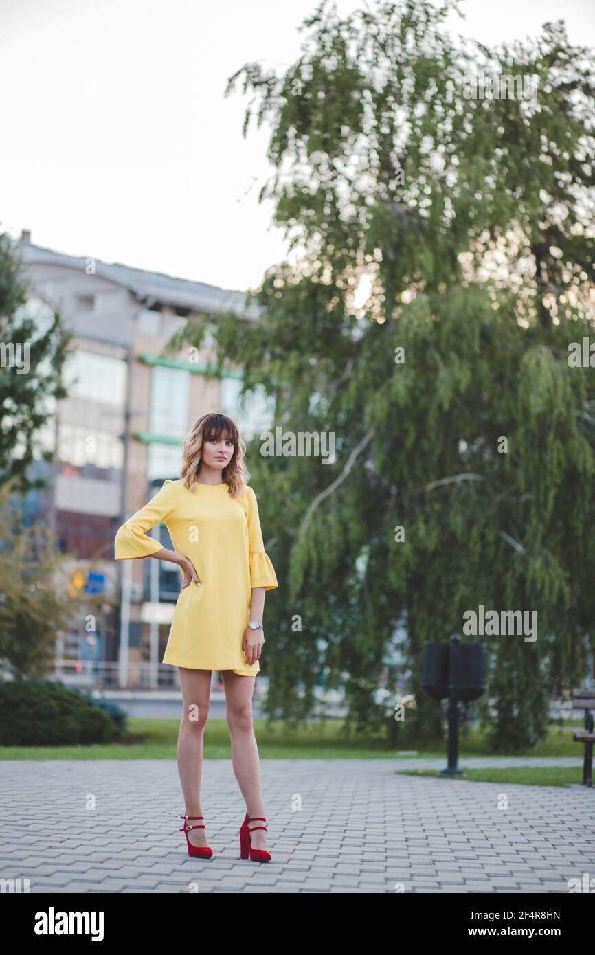 Attractive Caucasian woman wearing a yellow dress and red shoes in a park  Stock Photo - Alamy