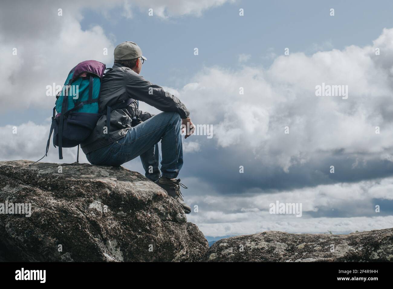 Tourist with backpack sits on the top of the mountain,resting and admiring the view from above.The concept of outdoor activities,travel and adventure. Stock Photo