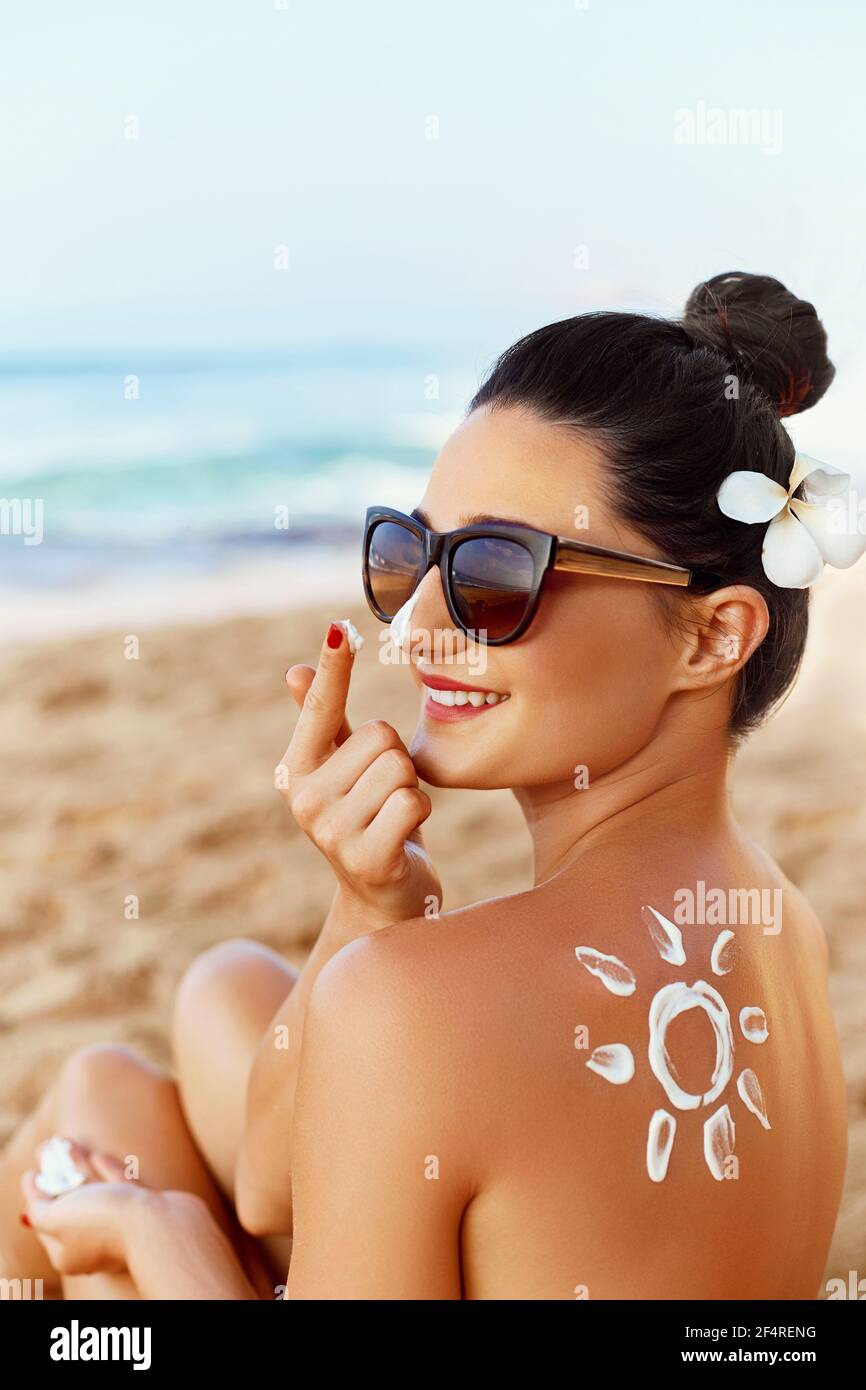 Attractive young woman traveler using skincare sunblock cream for sun protection on summer tropical beach lifestyle. Sunscreen lotion in sun shape on Stock Photo
