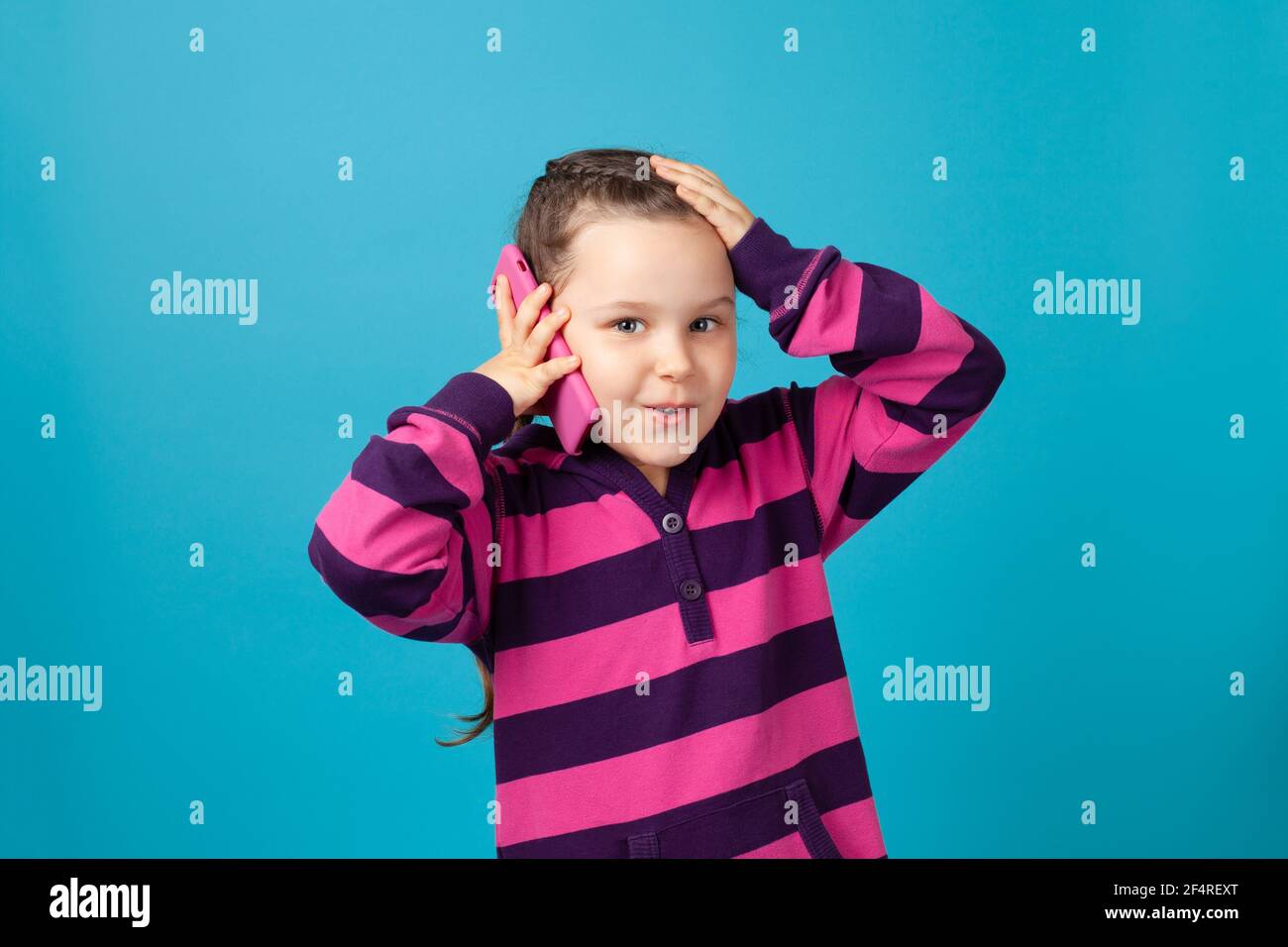 close-up portrait of surprised, shocked, delighted girl with pigtails making phone call and holding head with her hand isolated on a blue background Stock Photo