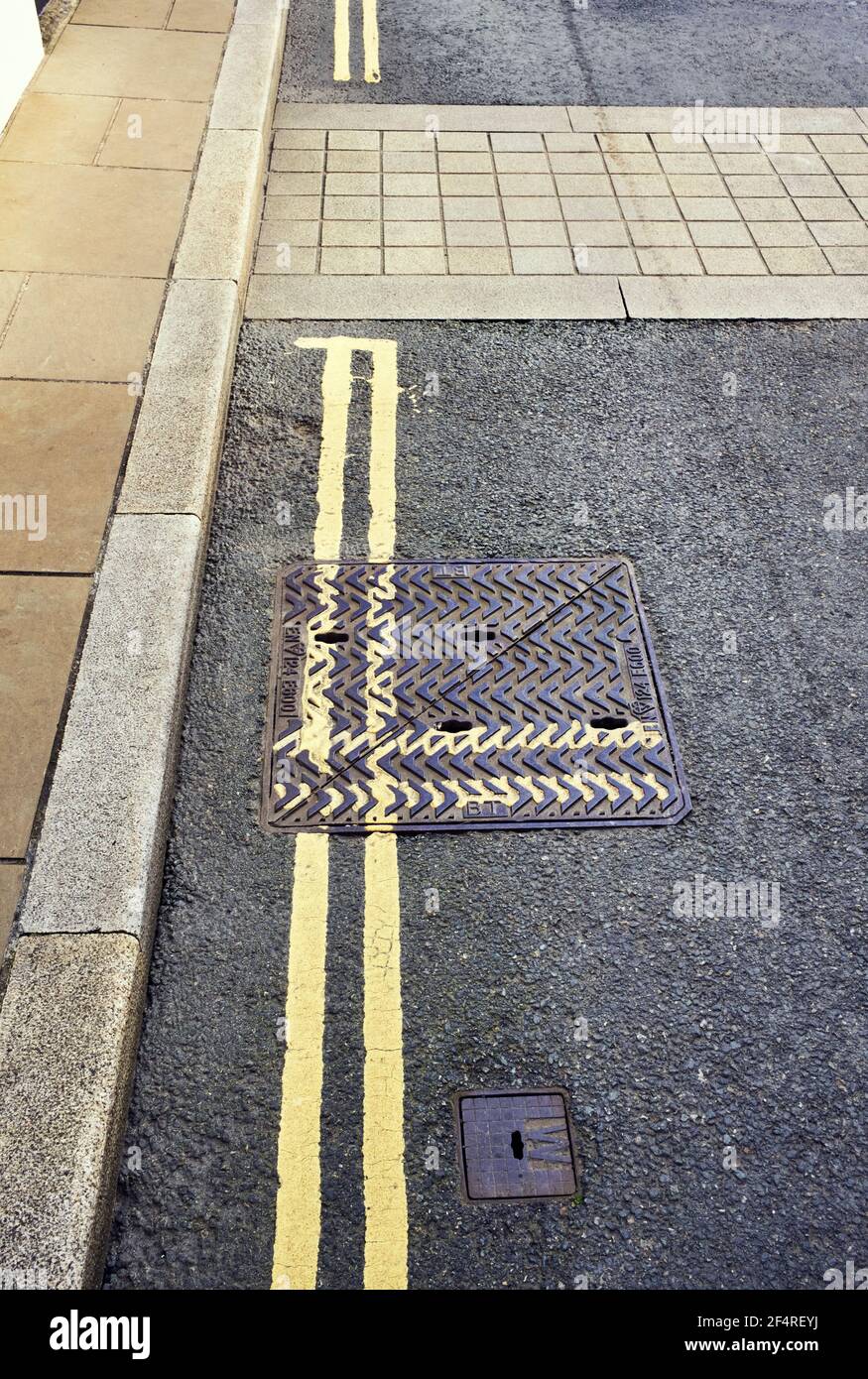 Drain cover with double yellow lines at ninety degrees to lines painted on the road Stock Photo