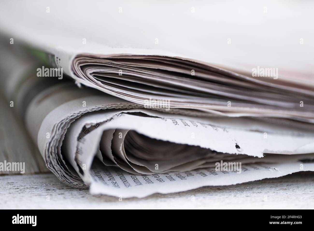 Folded newspapers with almost unreadable Dutch text on a table against plain background with narrow depth of field Stock Photo